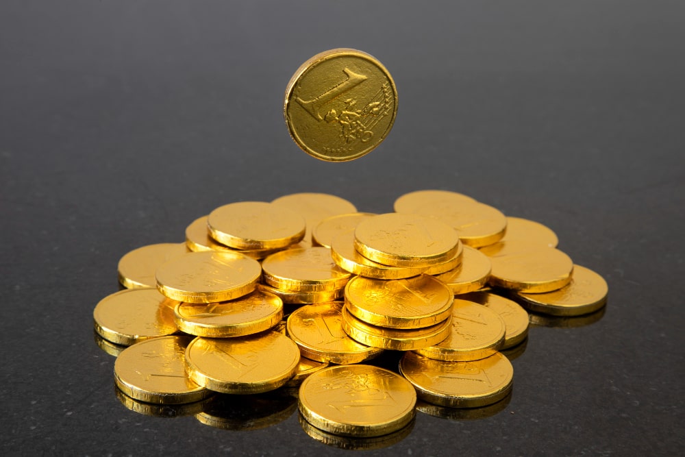 Un tas de pièces de chocolat dorées avec une pièce flottant au-dessus, évoquant l'idée de trésor et d'investissement.