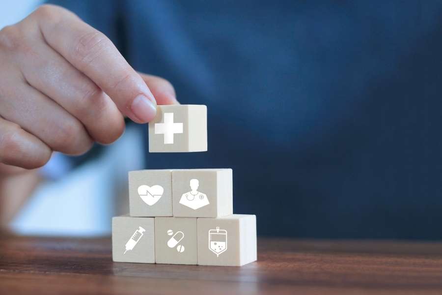 Une main dispose des blocs en bois avec des icônes médicales pour illustrer le fonctionnement d'une mutuelle modulable.
