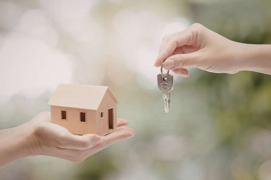 Une personne tient une petite maison en bois pendant qu'une autre lui tend des clés, idéal pour illustrer comment investir dans les petites surfaces.