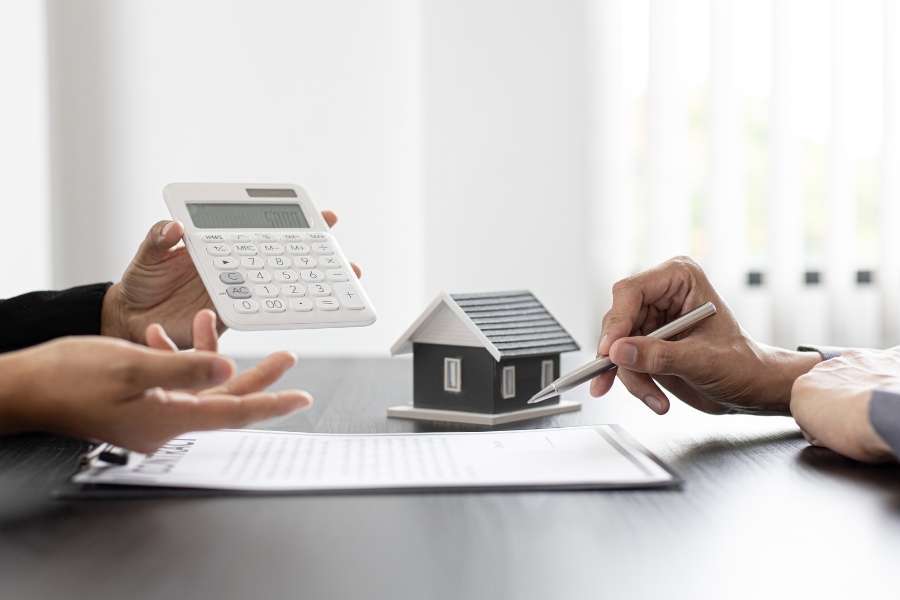 Deux personnes discutent des termes d'un contrat d'assurance habitation avec une maquette de maison sur la table.