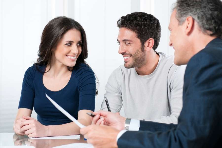 Un couple sourit en discutant avec un conseiller lors de la signature d'un contrat bancaire.