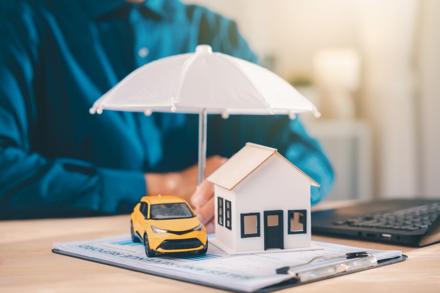 Une maquette de maison et une voiture miniature sous un petit parapluie sur des documents, illustrant le calcul d'une prime d'assurance habitation et auto.
